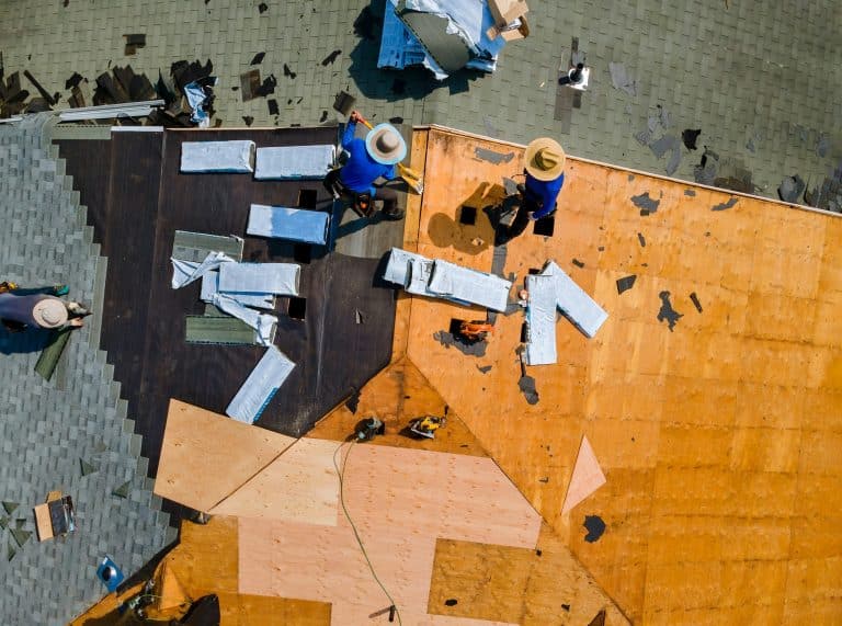 Worker hands installing bitumen roof shingles with air hammer and nail